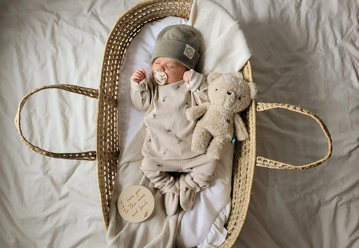 nouveau-né dormant paisiblement dans un lit-panier accompagné de son ourson en peluche